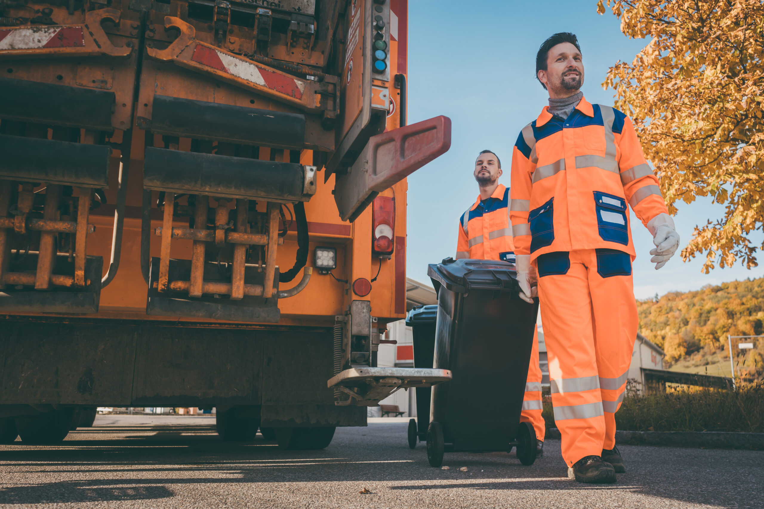 A garbageman walking towards the camera with a truck in the background.